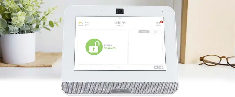 Smart security touchscreen panel showing the system disarmed, on a table beside a plant and reading glasses